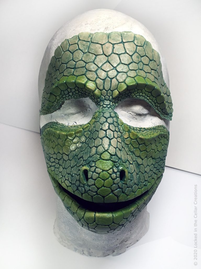 The Reptile face mask + makeup combo comes standard with black elastics on the mask that go around the head. The forehead prosthetic has to be glued on.